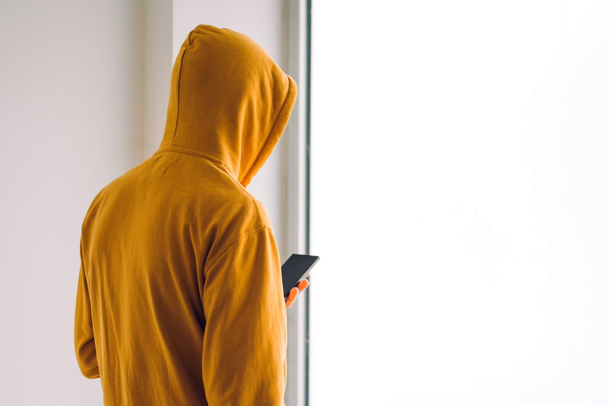 Man with hoodie and mobile phone standing by the window