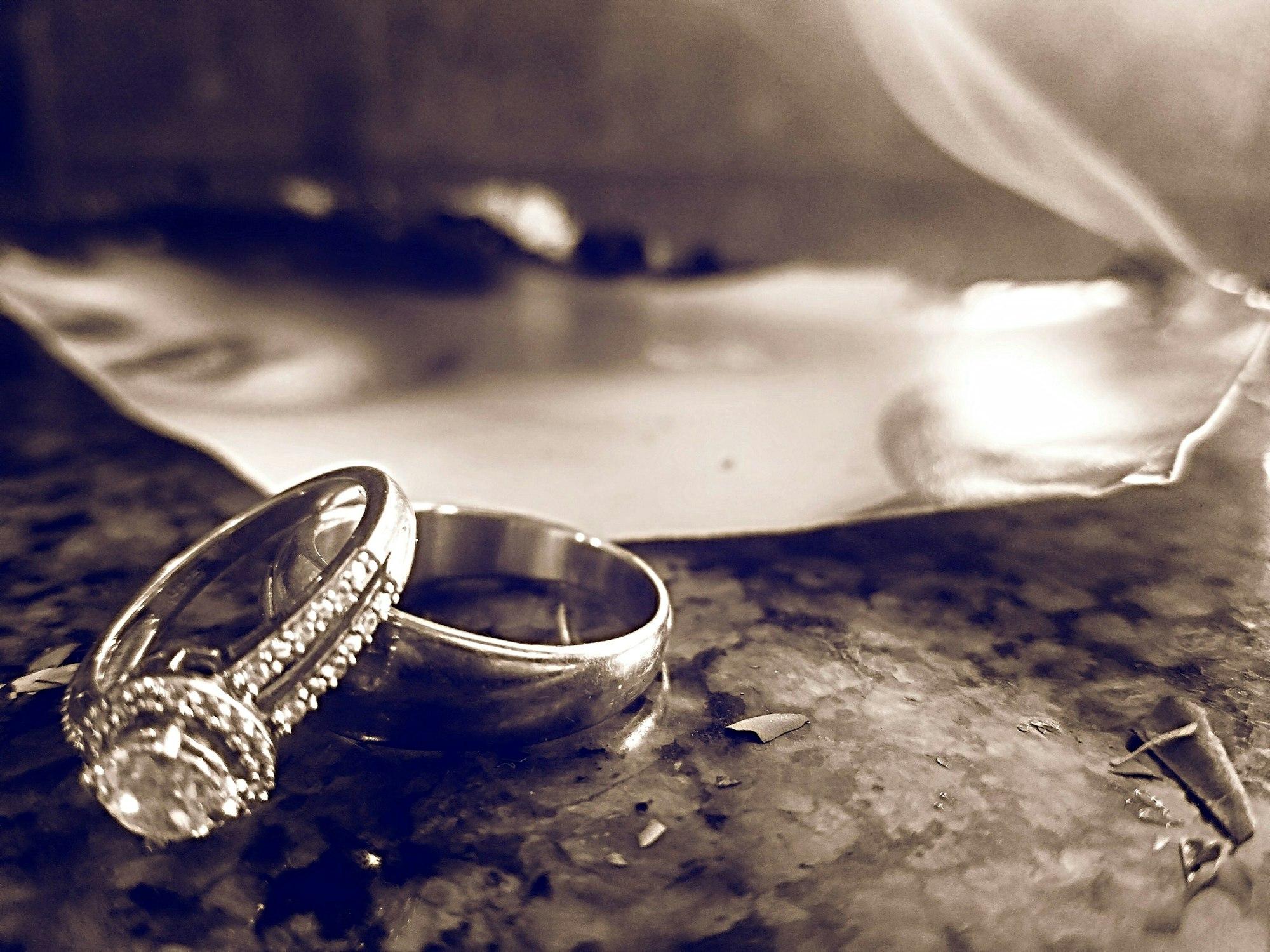Monochromatic image of torn photograph burning on countertop with wedding rings next to it.