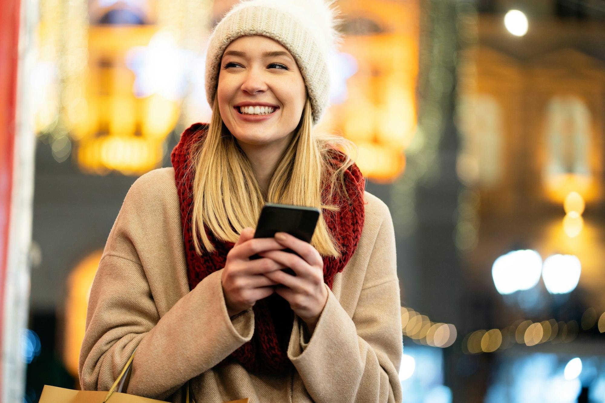 Portrait of young smiling beautiful woman using smartphone on the street at winter